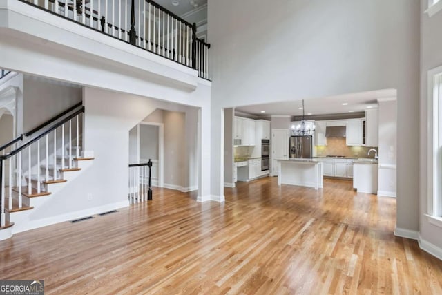 unfurnished living room with light wood finished floors, a towering ceiling, visible vents, and baseboards