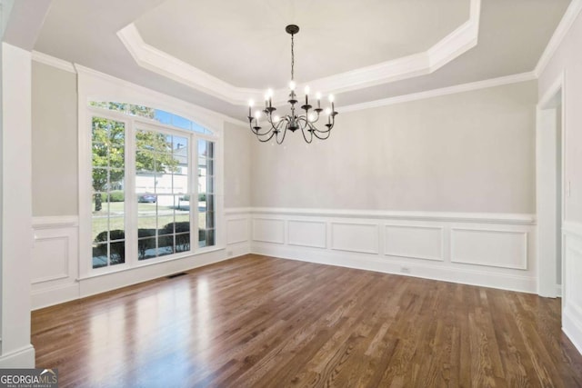 unfurnished dining area featuring visible vents, a chandelier, a raised ceiling, and wood finished floors