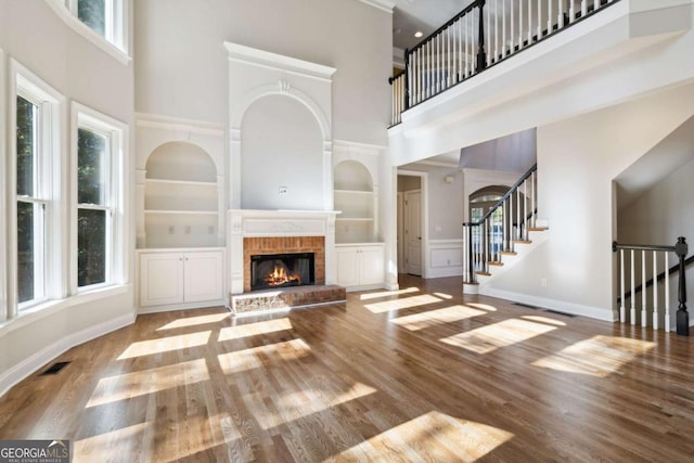 unfurnished living room featuring a fireplace, wood finished floors, baseboards, stairs, and built in features