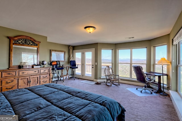 carpeted bedroom with access to outside, multiple windows, visible vents, and a mountain view