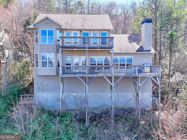 back of property with a wooden deck, a chimney, and a shingled roof