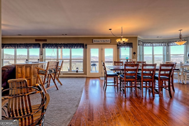 dining area with a notable chandelier, a healthy amount of sunlight, wood finished floors, and ornamental molding