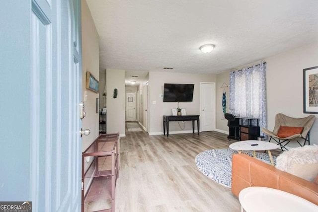 living room featuring light wood-type flooring, visible vents, baseboards, and a textured ceiling