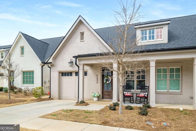 view of front of house featuring driveway, a porch, a shingled roof, a garage, and brick siding