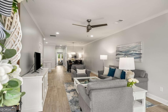 living room featuring light wood-type flooring, visible vents, crown molding, baseboards, and ceiling fan