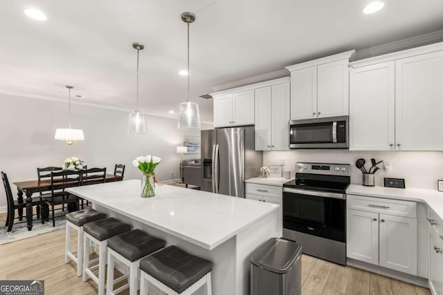 kitchen with appliances with stainless steel finishes, light wood-style flooring, a center island, and light countertops