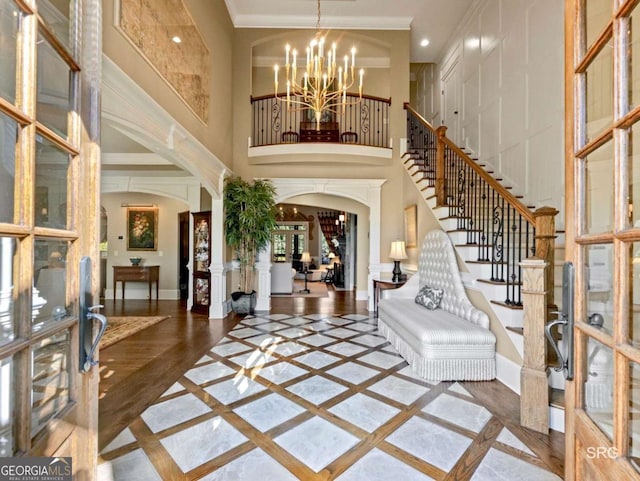 foyer with arched walkways, baseboards, ornamental molding, stairway, and an inviting chandelier