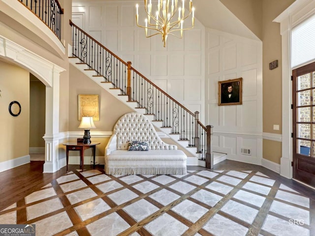 foyer entrance with a decorative wall, a high ceiling, visible vents, baseboards, and stairs