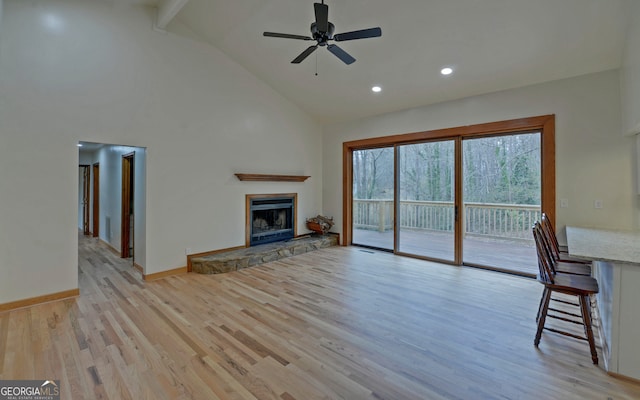 unfurnished living room featuring a fireplace, ceiling fan, high vaulted ceiling, light wood-type flooring, and baseboards