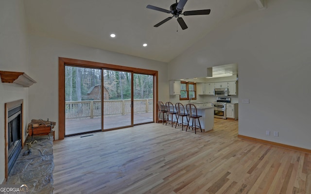 unfurnished living room featuring high vaulted ceiling, light wood-type flooring, a fireplace with raised hearth, and baseboards