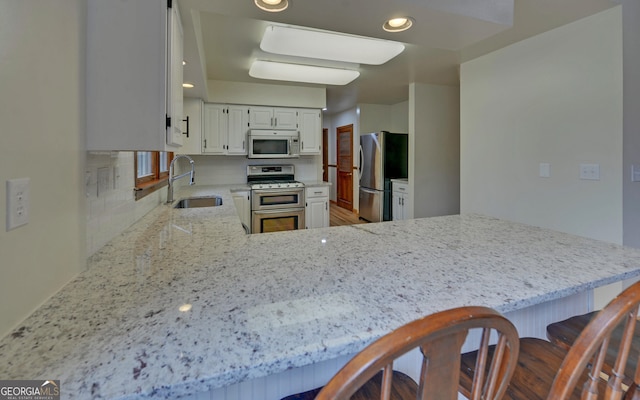 kitchen with light stone counters, stainless steel appliances, a peninsula, a sink, and decorative backsplash