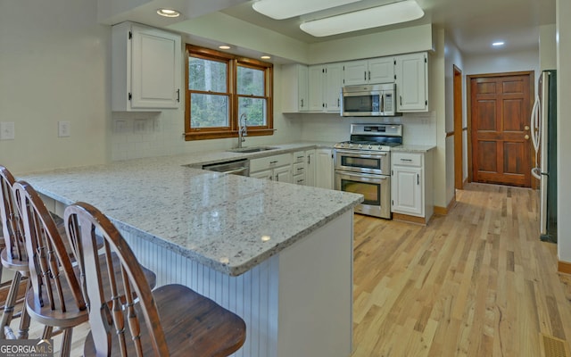 kitchen featuring light stone counters, a peninsula, stainless steel appliances, light wood-type flooring, and a sink