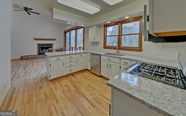 kitchen featuring dishwasher, light wood-style flooring, a peninsula, a fireplace, and a sink