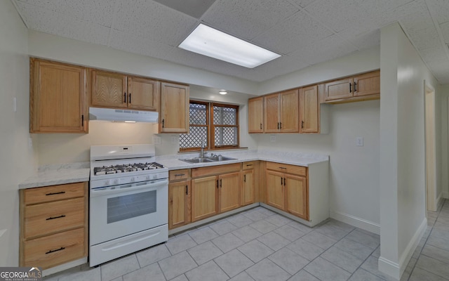 kitchen featuring a drop ceiling, under cabinet range hood, a sink, baseboards, and white range with gas cooktop