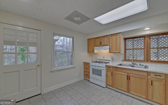 kitchen featuring a drop ceiling, light countertops, white gas stove, under cabinet range hood, and a sink