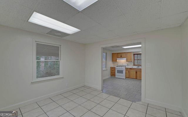 kitchen with light tile patterned floors, white range with gas cooktop, light countertops, a paneled ceiling, and a sink