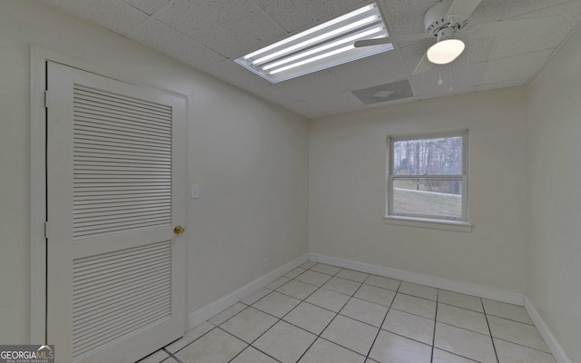 empty room with a drop ceiling, ceiling fan, baseboards, and light tile patterned flooring