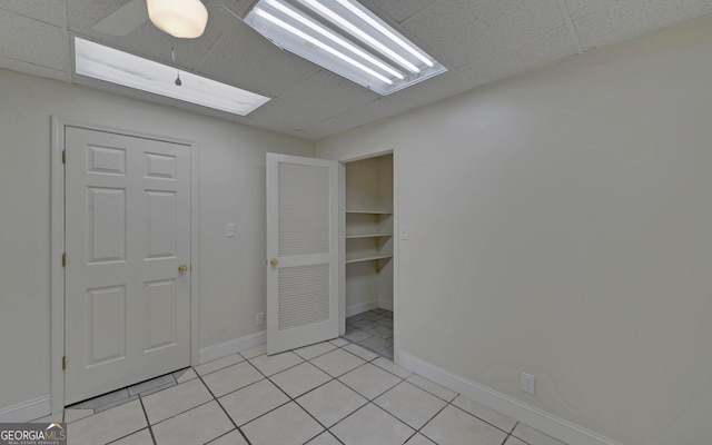 unfurnished bedroom featuring a drop ceiling, baseboards, and light tile patterned floors