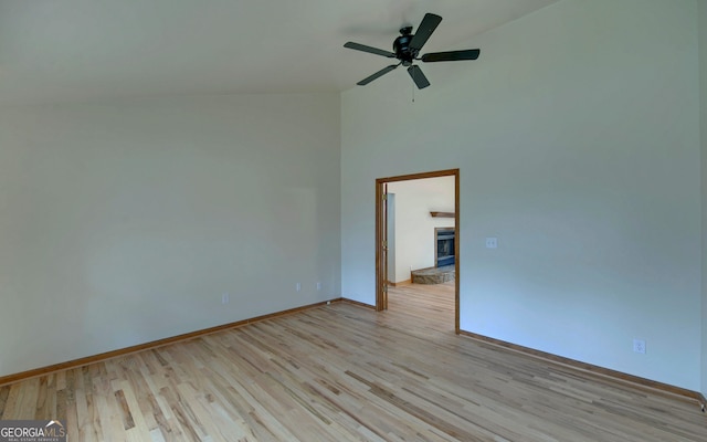 spare room featuring light wood-style flooring, a high ceiling, ceiling fan, a stone fireplace, and baseboards