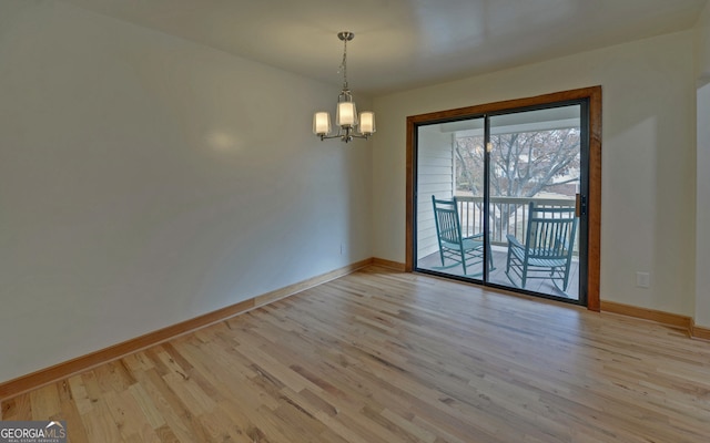 empty room featuring a chandelier, baseboards, and wood finished floors