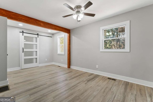 empty room featuring beam ceiling, visible vents, light wood finished floors, and a barn door