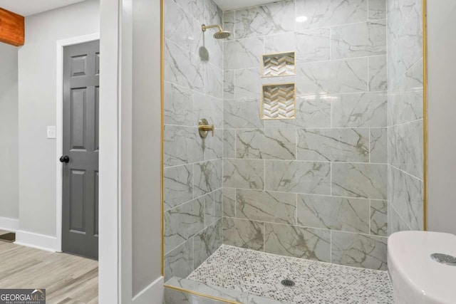 bathroom featuring toilet, baseboards, a tile shower, and wood finished floors