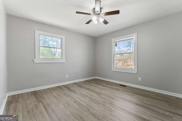 spare room featuring a ceiling fan, visible vents, baseboards, and wood finished floors