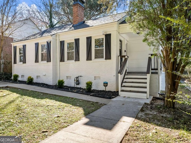 view of home's exterior with brick siding, a chimney, a lawn, entry steps, and crawl space