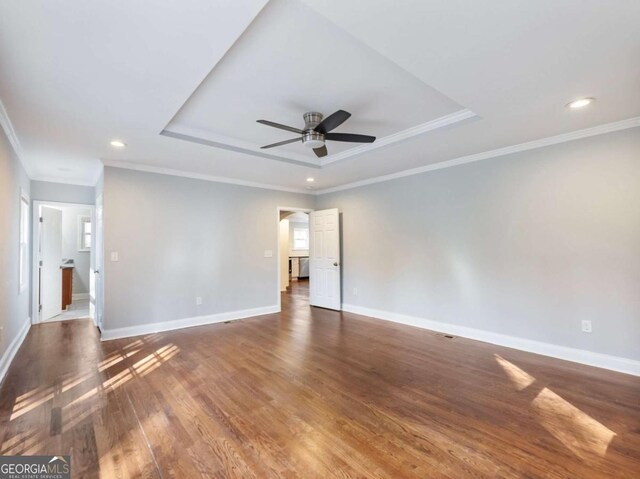 spare room featuring crown molding, recessed lighting, a raised ceiling, wood finished floors, and baseboards