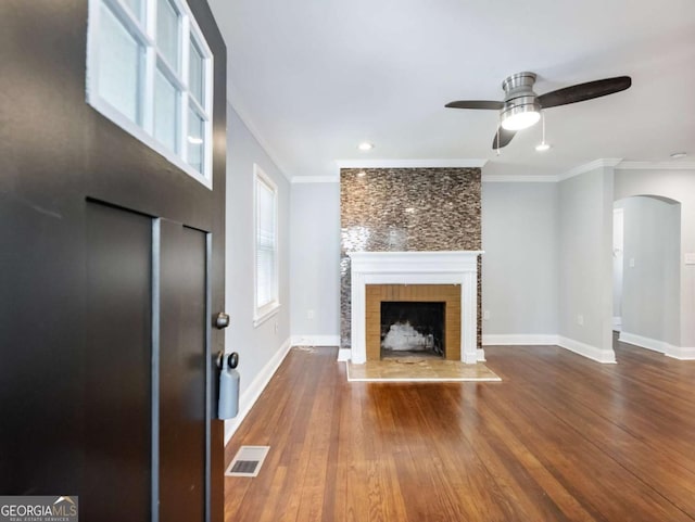 unfurnished living room with a fireplace with raised hearth, ornamental molding, wood finished floors, and visible vents