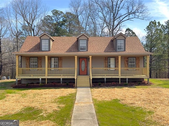 new england style home with covered porch, a shingled roof, and a front yard