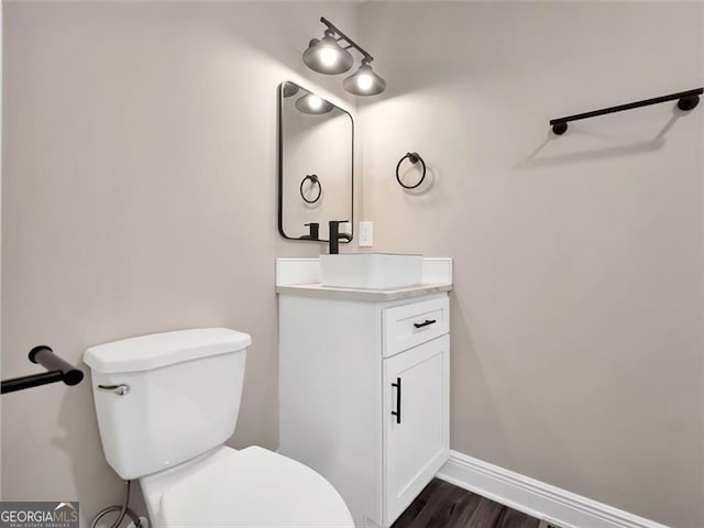 half bath featuring toilet, vanity, baseboards, and wood finished floors