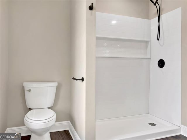 bathroom featuring toilet, baseboards, tiled shower, and wood finished floors