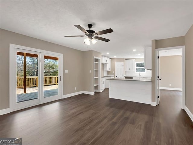 unfurnished living room featuring dark wood-style floors, a sink, a ceiling fan, and baseboards