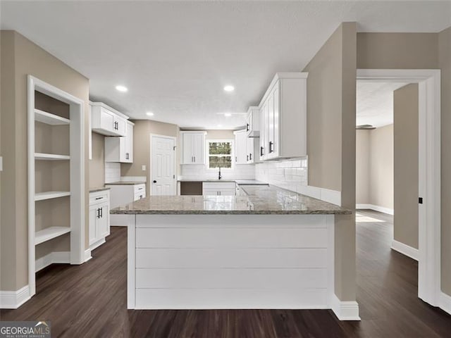 kitchen with a peninsula, baseboards, white cabinets, light stone countertops, and dark wood-style floors