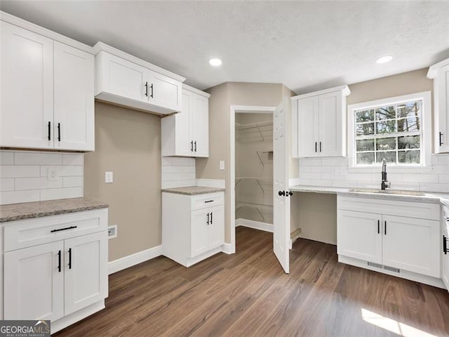 kitchen featuring dark wood-style flooring, a sink, white cabinetry, baseboards, and light stone countertops