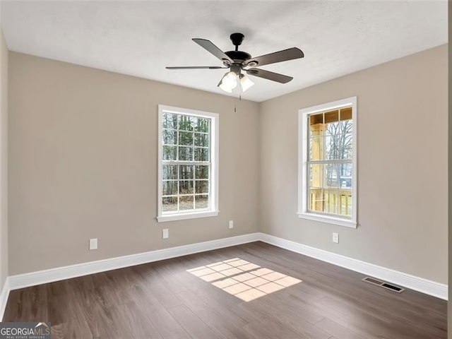 empty room with dark wood-type flooring, visible vents, ceiling fan, and baseboards