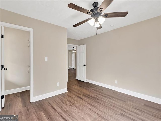 unfurnished bedroom with a ceiling fan, a walk in closet, baseboards, and wood finished floors