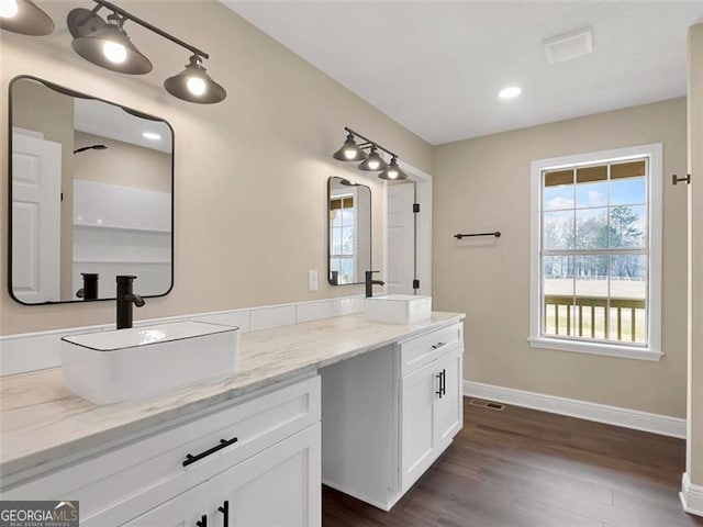 bathroom featuring wood finished floors, a sink, baseboards, and double vanity