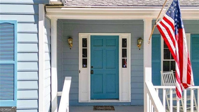 entrance to property featuring covered porch and roof with shingles