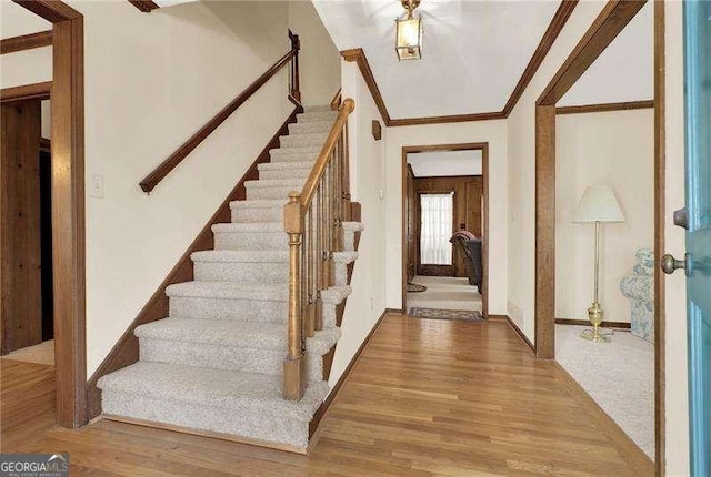 foyer entrance with ornamental molding, stairway, wood finished floors, and baseboards