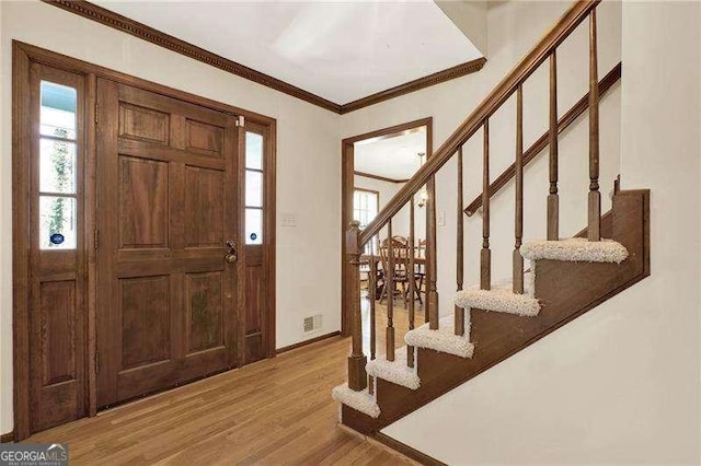 entrance foyer with wood finished floors, visible vents, baseboards, stairs, and ornamental molding