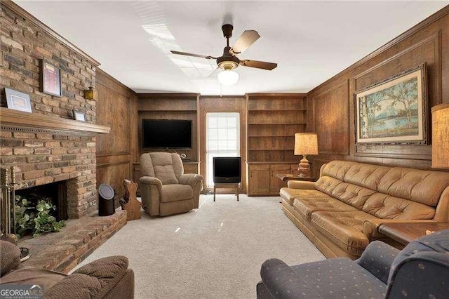 living area with ceiling fan, wooden walls, light carpet, built in features, and a brick fireplace