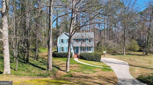 view of front facade with driveway, a front lawn, a balcony, and a view of trees