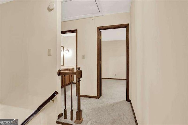 hall featuring attic access, light colored carpet, an upstairs landing, and baseboards