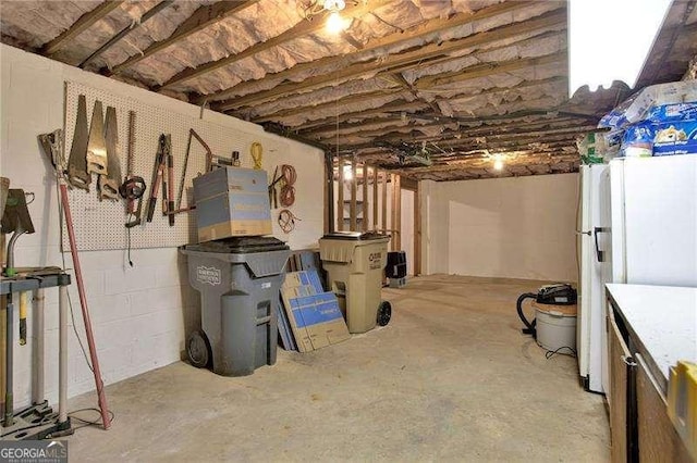 unfinished basement featuring freestanding refrigerator and concrete block wall