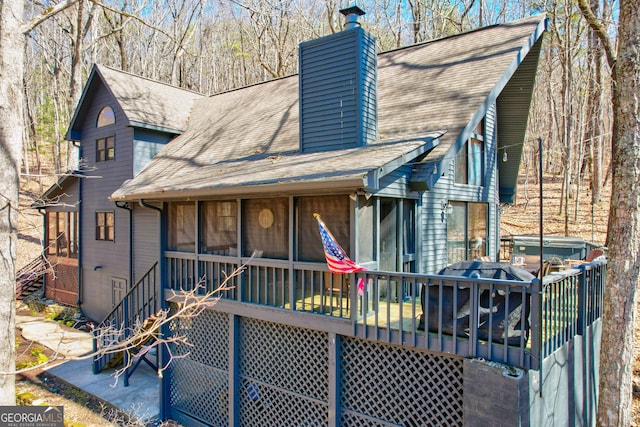 view of front facade with a shingled roof, a sunroom, a chimney, and a deck