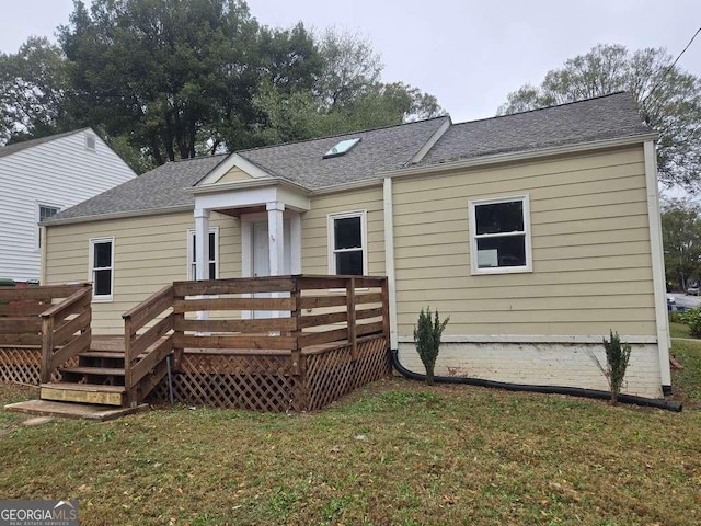 back of property featuring a wooden deck, a lawn, and roof with shingles