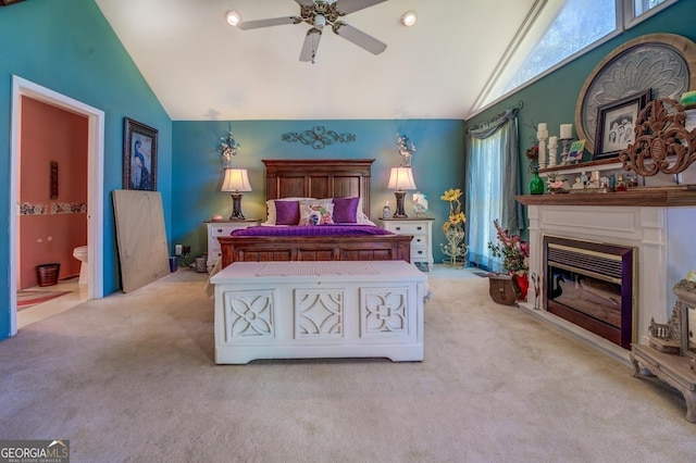 carpeted bedroom featuring high vaulted ceiling, ensuite bathroom, a ceiling fan, and a glass covered fireplace