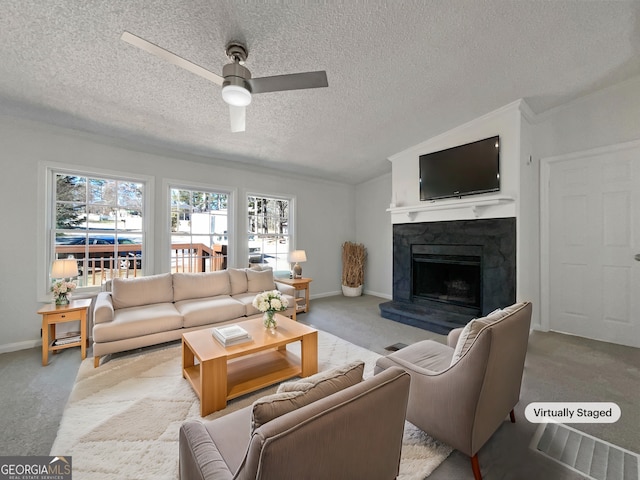 carpeted living area with a textured ceiling, baseboards, a fireplace with raised hearth, and a ceiling fan